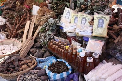 Display of traditional medicine in a Madagascar marketplace. Baskets are full of roots, dried plants, and there are jars filled with an amber liquid.