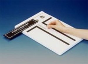 A hand using a tactile graphics tool on a white board with black raised lines, likely for creating or reading braille or tactile graphics. No visible text or math content is present.
