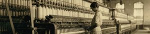 A person working in a textile factory stands beside a large machine with multiple spools of thread. The industrial setting includes rows of similar machinery extending into the background.