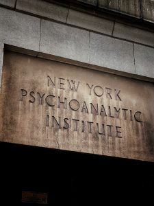 Entrance of a building with the words "NEW YORK PSYCHOANALYTIC INSTITUTE" engraved above the doorway on a stone or concrete surface.