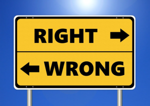 A yellow road sign with two sections. The top section has the word RIGHT in black capital letters with a right-pointing arrow. The bottom section has the word WRONG in black capital letters with a left-pointing arrow. The sign is set against a blue sky background with a bright light source at the top center of the image.