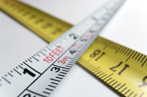 Two measuring tapes crossed over each other—one white with black and red markings showing measurements in feet and meters, and one yellow with black markings showing measurements in inches.