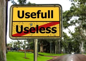 A road sign with "Usefull" in black text on a yellow background at the top, and "Useless" crossed out with a red diagonal line. The sign is set against a tree-lined road.