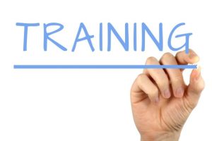 The word "TRAINING" written in large blue letters, with a hand holding a blue marker drawing an underline beneath the word.